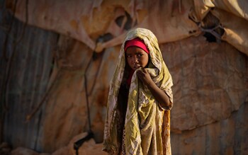 A young Somali girl stands outside her makeshift hut at a camp of people displaced from their homes elsewhere in the country by the drought