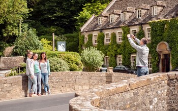 Tourists posing in the Cotswold village of Bibury, Gloucestershire, UK